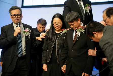 SCC Executive Secretary Danny Chan prays the ordination prayer as ordained ministers in attendance lay hands on Zhang and his wife.