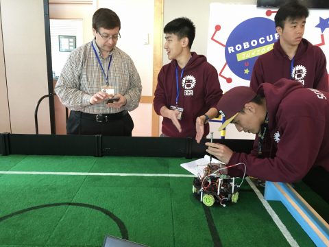 Maxon Zhao (second from left) assists Chris Kmosko from another division’s team, with some technical information, while Watchara Lu (right) makes some adjustments on SGA’s robot. Photo by Prakash Rajendran and Raiden Yang