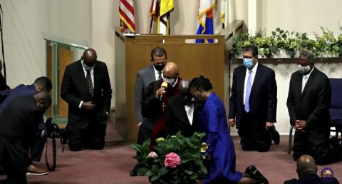 Conference leadership and pastors in attendance bow as Royal Harrison, SCC Greater Los Angeles Region director, prays the ordination prayer over Barksdale and his wife, Sonia.