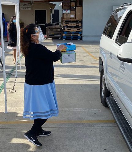 A member from East Los Angeles Bilingual church hands gifts to a family in their car.