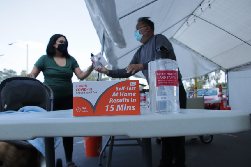 Melendez (right) shares COVID rapid selftest kits and hand sanitizer with a neighbor from the community.