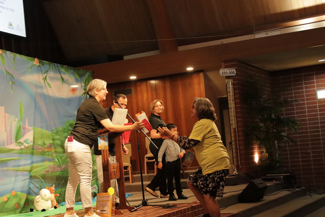 An attendee (right) accepts her raffle ticket prize: a JBL Flip Portable Bluetooth Speaker.