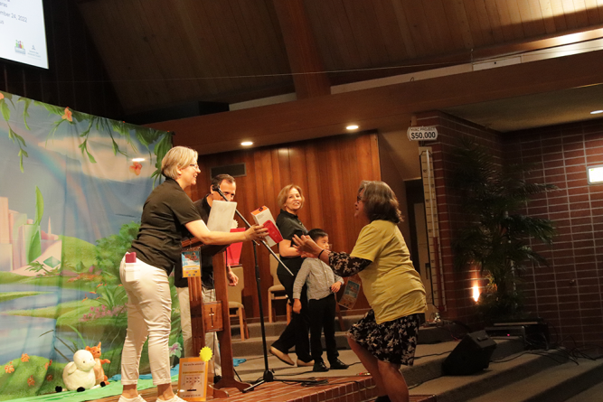 An attendee (right) accepts her raffle ticket prize: a JBL Flip Portable Bluetooth Speaker. 