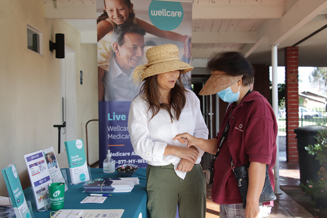 Two attendees discuss Wellcare Medicare insurance after taking a business card from a representative.