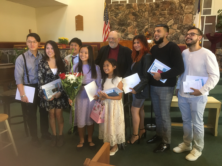 Newly baptized members of Sylmar church gather for a photo with Aitken (center), holding their new Bibles and certificates. (Left to right, front row) Mitchell Won, Tiffanie Pham, Joash Adlawan, Zyana Juan, Kysha Lastima, (left to right, back row) Destiny Fuentes, Adrienne Loaiza, and Michael Duarte.