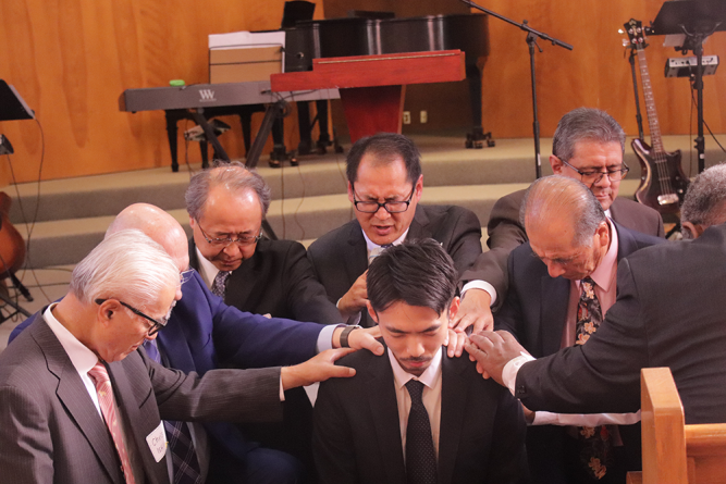 Ordained pastors lay hands on Shinasue during the ordination prayer.