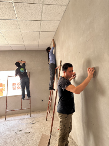 The team sands and washes the walls with materials they have on hand: bricks for sanding and cut-up jeans for washing.