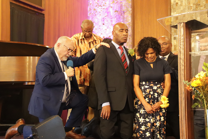Ordained pastors lay hands on Baptiste and his wife as Cress offers the ordination prayer.